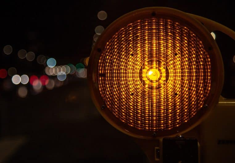 Gyrophare jaune sur route de nuit avec cônes et halo lumineux.