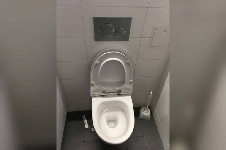 Toilettes d’aéroport en Finlande, brosse posée à côté de la cuvette.