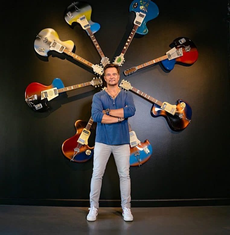 Portrait en plan moyen de David Hallyday debout, photographié à Monaco, fond sombre et éclairage de scène.