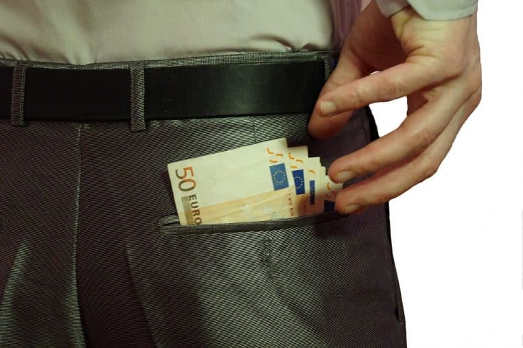 Main glissant des billets en euros dans la poche arrière d’un pantalon, évoquant un don ou versement discret en espèces.