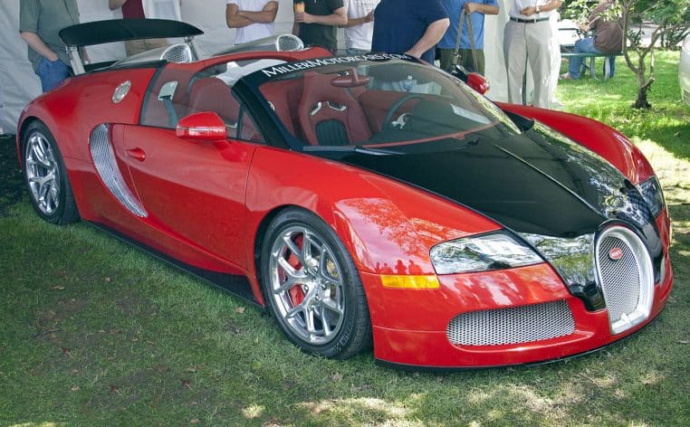 Bugatti Veyron Grand Sport rouge et noire exposée en extérieur sur une pelouse, vue de trois-quarts avec la capote ouverte et l’habitacle en cuir.