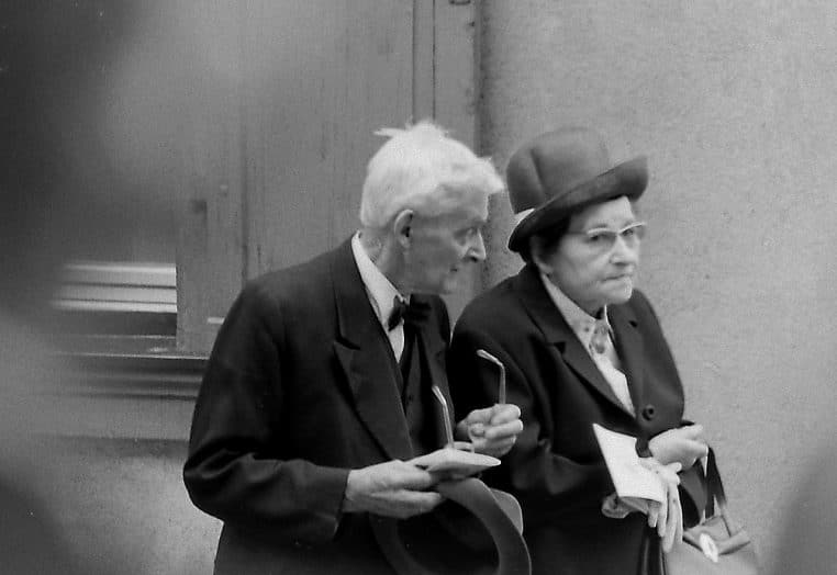 Couple âgé marchant côte à côte lors d’une procession en plein air, symbole des retraités dans l’espace public européen.