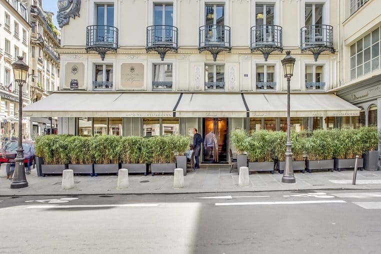 Façade du restaurant Drouant à Paris en plan horizontal, avec enseigne et terrasse visibles sur la rue, prise en journée depuis le trottoir.