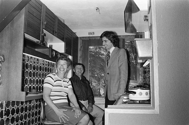 Cuisine des années 70 en noir et blanc avec éléments intégrés et rangements muraux, ambiance rétro authentique et lignes simples.