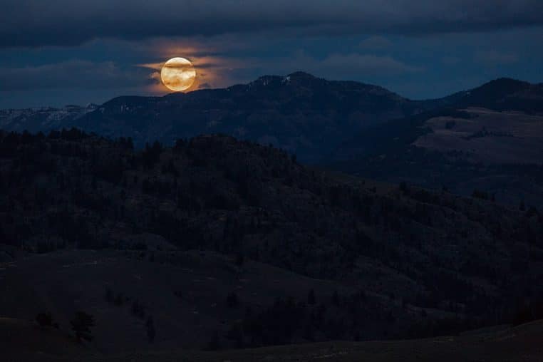Super Lune se levant sur Pleasant Valley au Yellowstone, reliefs sombres et disque lunaire lumineux à l’horizon.
