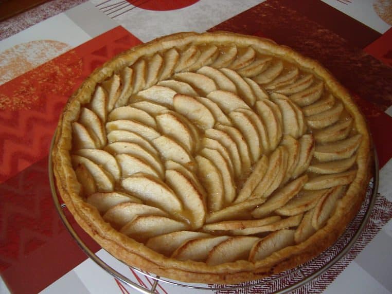 Tarte aux pommes dorée, rosace régulière et bordure feuilletée, vue rapprochée sur une grille.