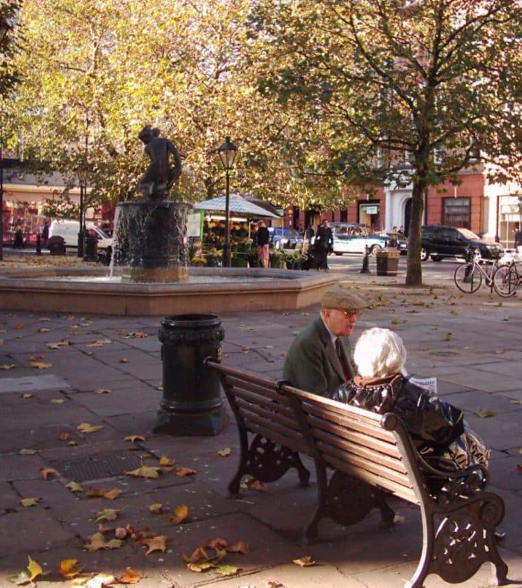 Couple de personnes âgées marchant sur une place de Londres, représentant des retraités européens en ville.