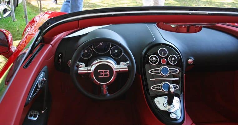 Intérieur d’une Bugatti Veyron Grand Sport rouge, cadré sur le volant, la console centrale et les commandes, dont les boutons de réglage.