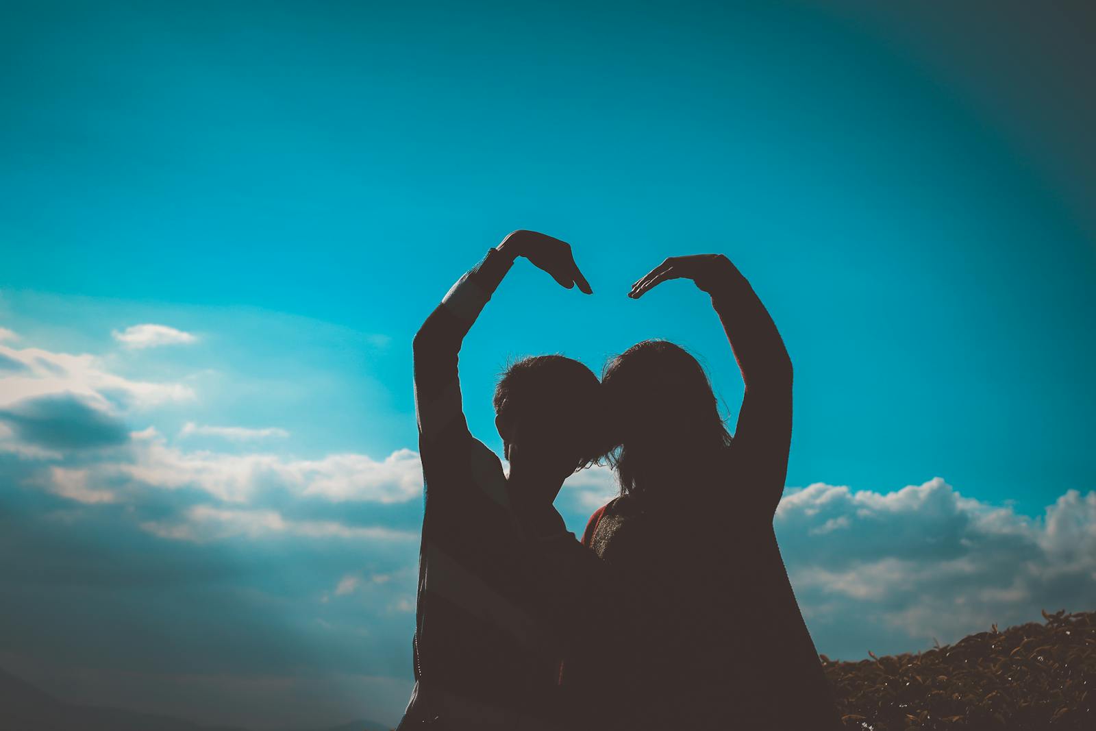 Silhouette of a couple creating a heart shape with their arms in a romantic outdoor setting.