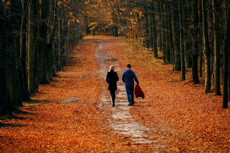 A couple walks along a leaf-covered forest path during a vibrant autumn day.
