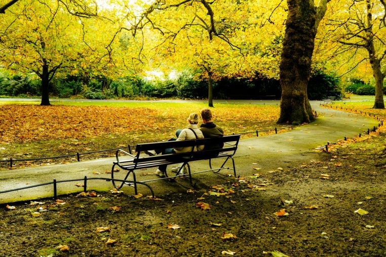 A couple enjoys a peaceful moment on a park bench surrounded by vibrant autumn leaves.
