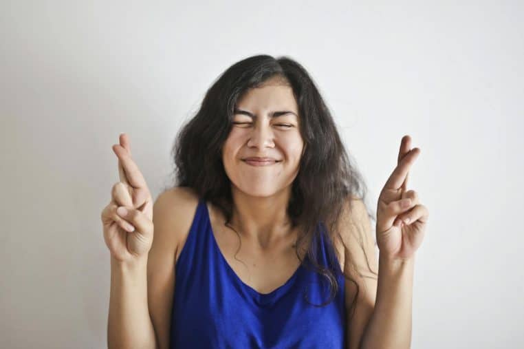 Happy woman with fingers crossed, expressing hope and good luck, on a white background.