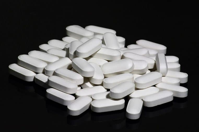 Gros plan sur un tas de comprimés blancs de supplément calcium-vitamine D posés sur une surface noire, illustrant la supplémentation quotidienne