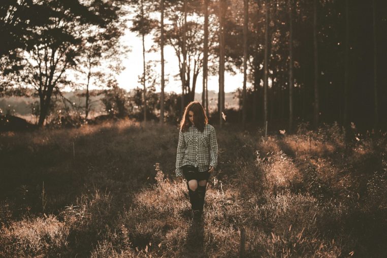 woman walking on brown grass field near trees