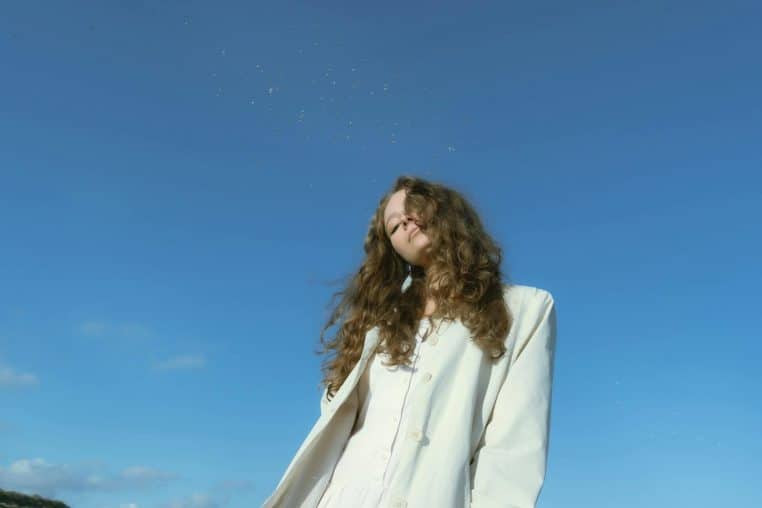 A woman with long hair stands confidently against a clear blue sky, embodying freedom and style.