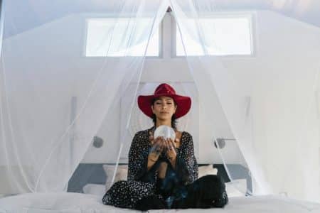 A woman wearing a red hat holds a crystal ball in an ethereal setting, suggesting mystery and magic.