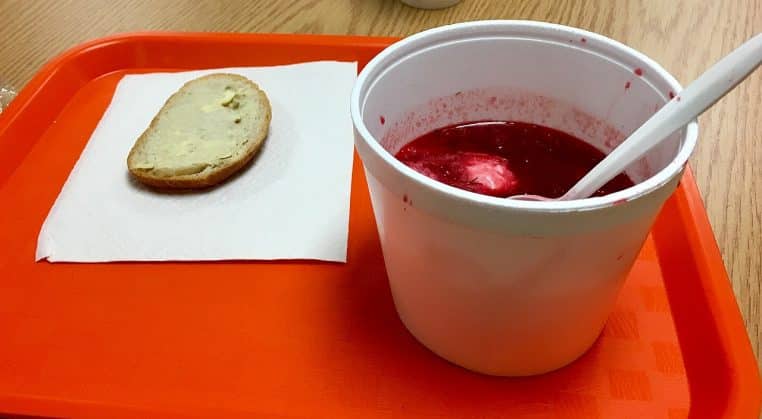 Bol de bortsch rouge servi avec une cuillerée de crème blanche au centre, posé sur une table avec couverts et serviette.