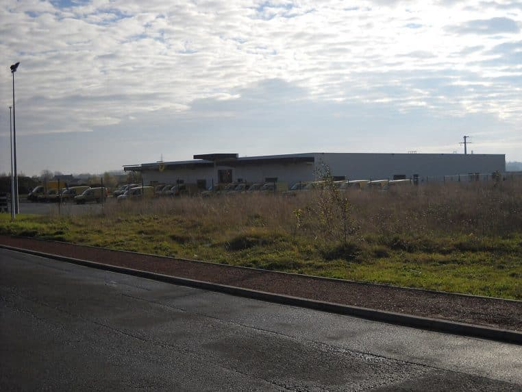Vue extérieure d’un centre de tri postal à Aire-sur-la-Lys, bâtiment sur parking, plan large en journée.