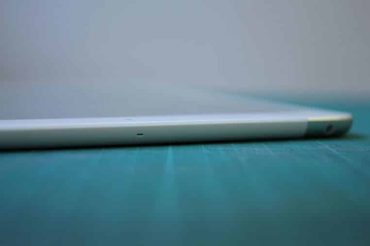 iPad Air tenu à deux mains par un utilisateur, écran vers le photographe, dans un cadre intérieur neutre et lumineux.