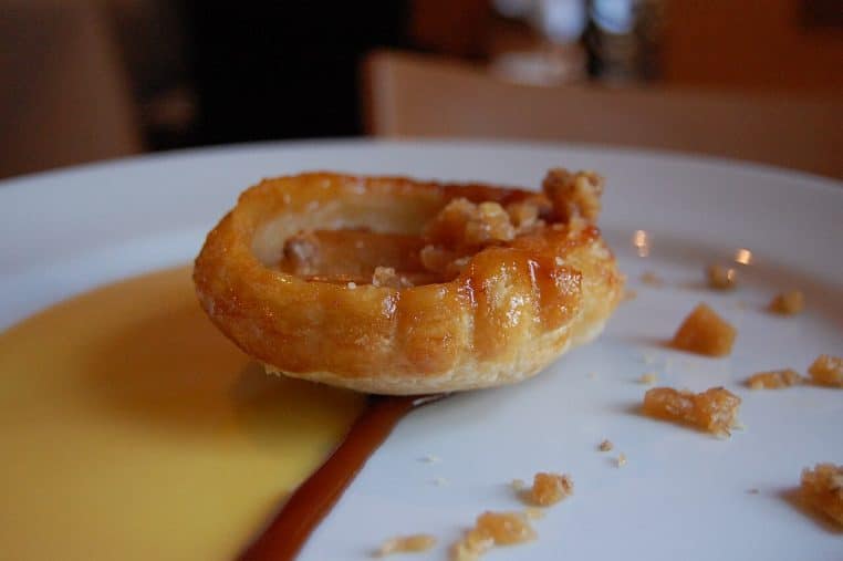 Petite tarte aux pommes nappée, posée dans une assiette avec sauce anglaise et trait de caramel.