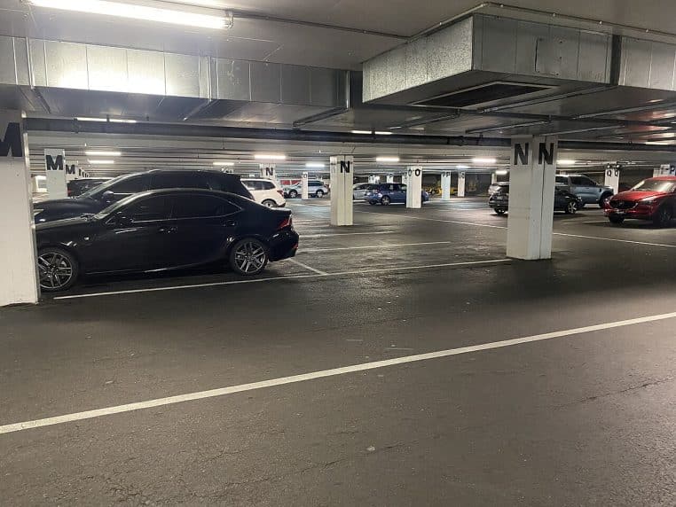 Parking souterrain de centre commercial avec rangées de voitures garées, colonnes numérotées et éclairage fluorescent.