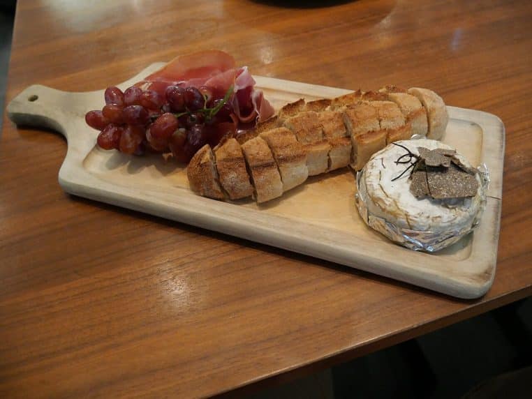 Camembert cuit au four servi avec pain et charcuterie, fromage coulant, photo serrée en lumière chaude