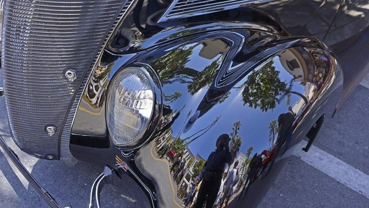 Gros plan sur une carrosserie noire brillante de voiture ancienne, avec courbes chromées typiques d’un coupé de collection américain.