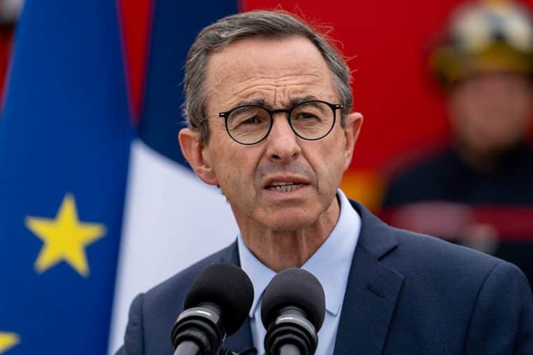 Bruno Retailleau parlant devant micros, drapeaux français et européen en arrière-plan, lors d’une allocution officielle.