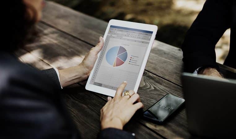 Gros plan sur un iPad montrant un graphique pendant une discussion de café, mains posées, cadrage horizontal net.