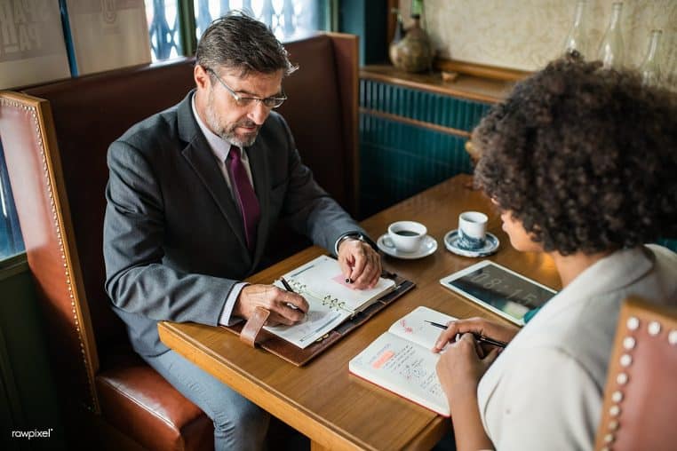 Deux personnes échangent au café avec ordinateur portable ouvert, graphique affiché, atmosphère de travail détendue et cadrage horizontal.