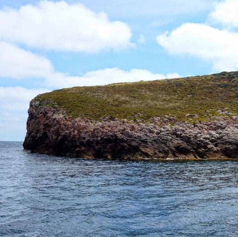 Côtes rocheuses de type baléare au bord d’une mer calme, eau bleu profond, végétation basse, rappelant le littoral préservé de Cabrera.