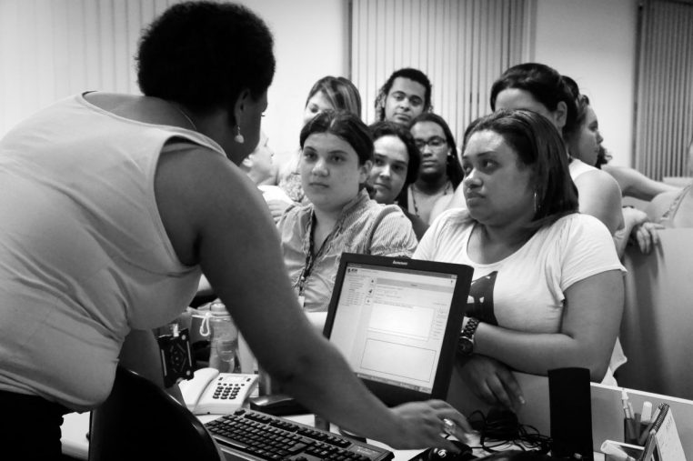 Employés rassemblés autour d’un poste informatique dans un open space de call center, représentant l’organisation des centres de démarchage téléphonique.