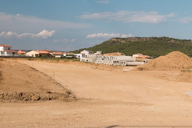 Terrain viabilisé avec voiries en chantier et réseaux apparents, avant construction des maisons, vu en large plan horizontal.