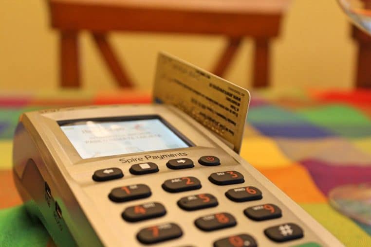 Gros plan sur un terminal de paiement et une carte glissée dans la fente, sur une table colorée, évoquant un achat du quotidien.