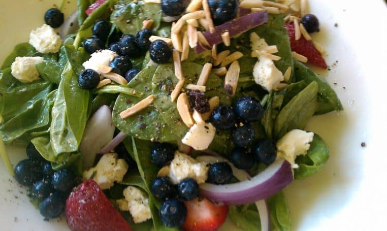 Salade de jeunes épinards avec myrtilles, fraises, fromage frais et amandes effilées, présentée en gros plan dans une assiette claire.