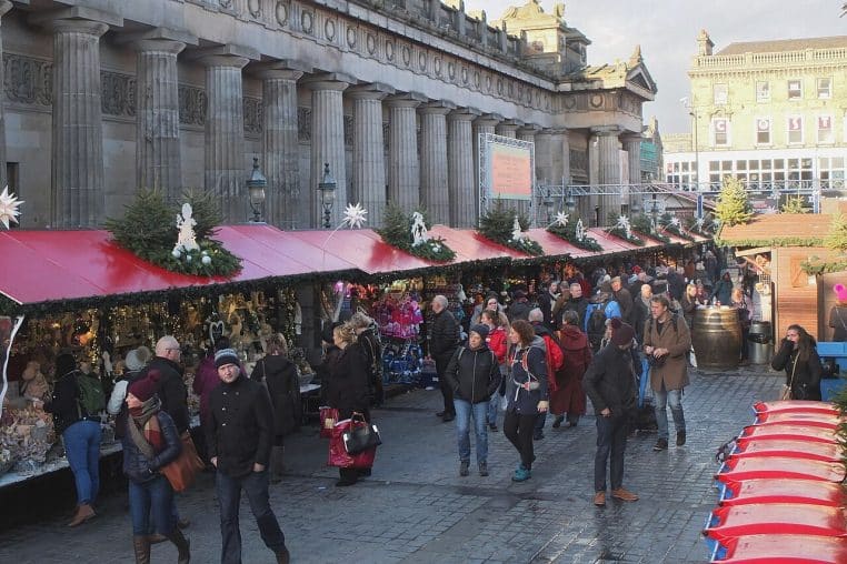Chalets du marché de Noël installés dans les jardins, grande roue illuminée et silhouettes de visiteurs sous le regard du château au loin.