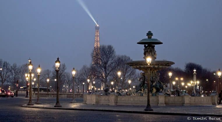 Fontaine et réverbères illuminés place de la Concorde à Paris en soirée hivernale, tour Eiffel au fond sous un ciel légèrement brumeux.