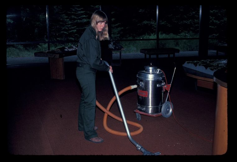 Agent d’entretien en train de laver un sol intérieur avec un aspirateur industriel à roulettes, câble déployé.