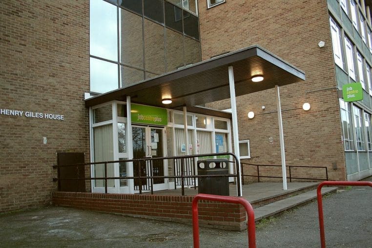 Façade d’un Jobcentre Plus en ville, avec enseigne verte bien visible, représentant un service public chargé du suivi des chômeurs.