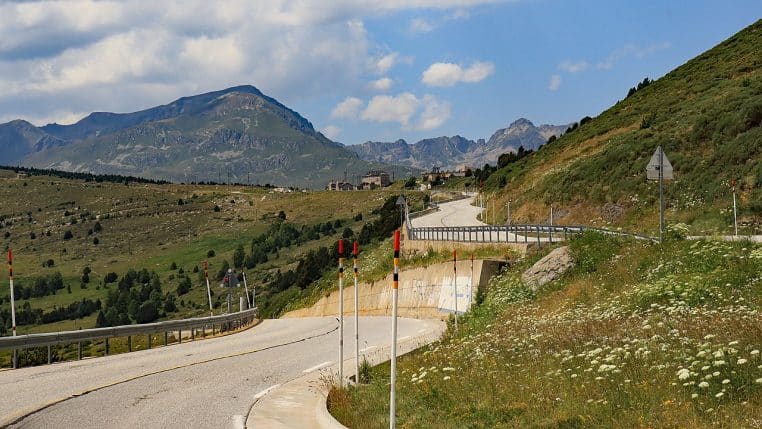 Grand paysage horizontal du Col de Puymorens avec lacet routier, versants poudrés et ciel limpide.