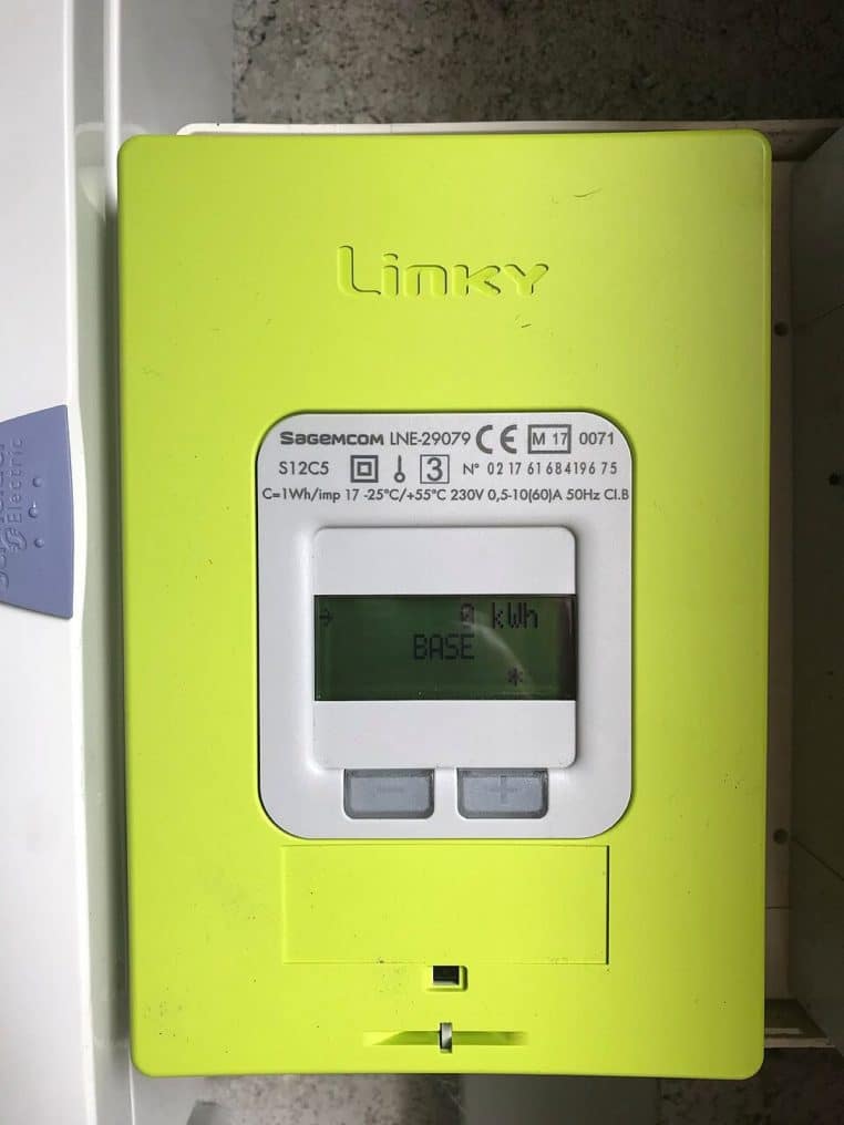 Compteur Linky jaune-vert fraîchement installé sur une planche bois au mur d’un logement en France, alimentation visible.