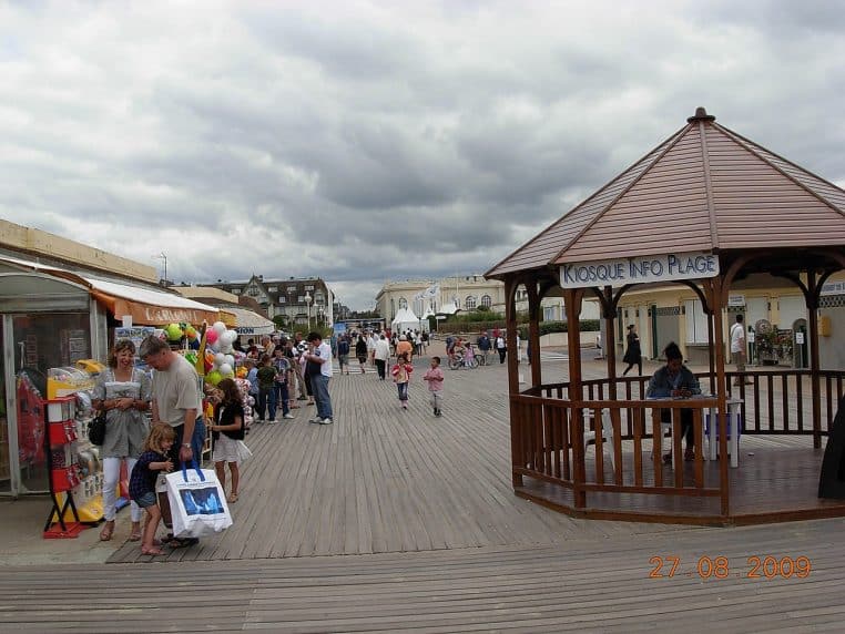 Les Planches de Deauville sous ciel clair, perspective sur le front de mer et les cabines emblématiques baignées de lumière.