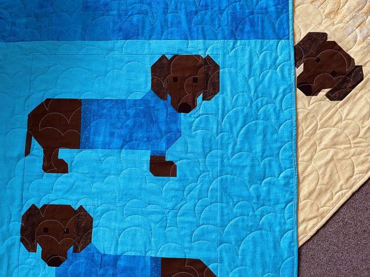 Gros plan sur un motif textile montrant des dachshunds portant des pulls d’hiver colorés, illustrant l’esprit des pulls de Noël.