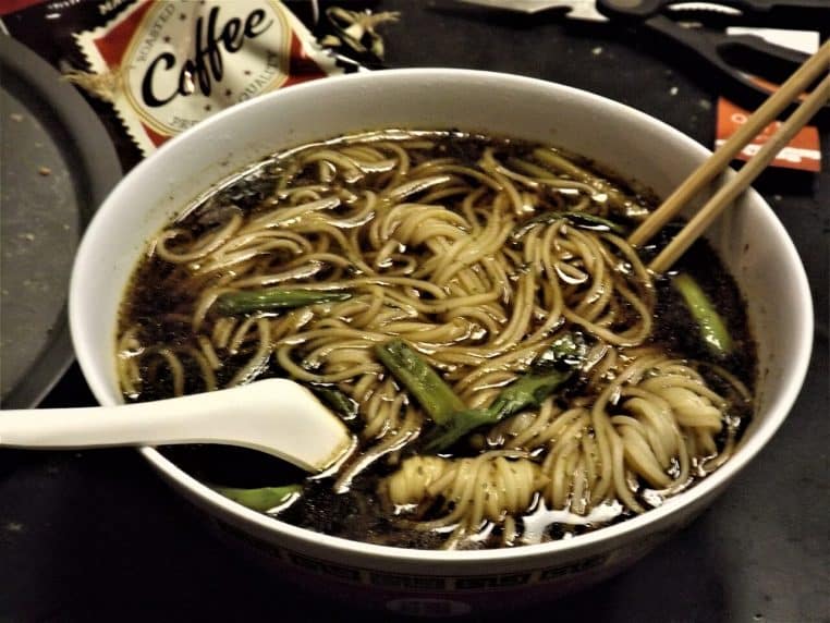 Bol de nouilles fines à la sauce soja posé sur une table, accompagné de bouillon et de légumes, évoquant une assiette de pâtes simple mais très savoureuse.