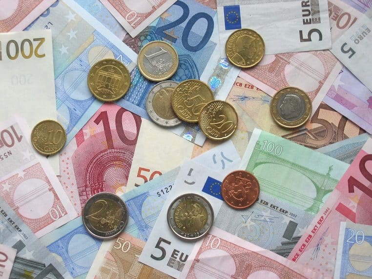 Billets et pièces en euros étalés sur une surface, dont un billet de 5 euros au milieu d’un mélange de valeurs différentes