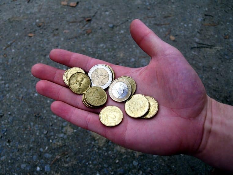 Gros plan horizontal d’une main tenant plusieurs pièces en euros, image concrète de l’épargne européenne.