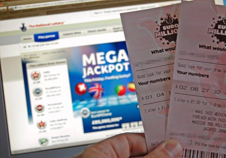 Gros plan sur deux tickets EuroMillions tenus devant un écran affichant un Mega Jackpot, scène typique d’achat de grille avant tirage