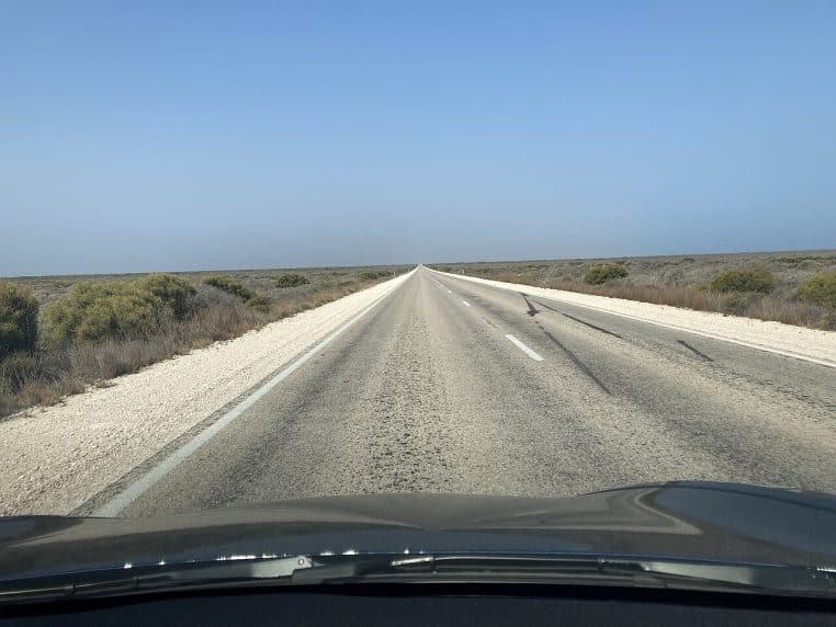 Route rectiligne traversant un plateau désertique austral, vue depuis l’intérieur d’une voiture sous un ciel parfaitement dégagé.