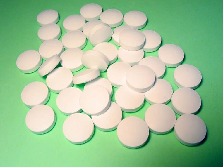 Comprimés ronds blancs disposés sur un fond vert, représentant une cure de vitamine D3 sous forme de petites pastilles anonymes