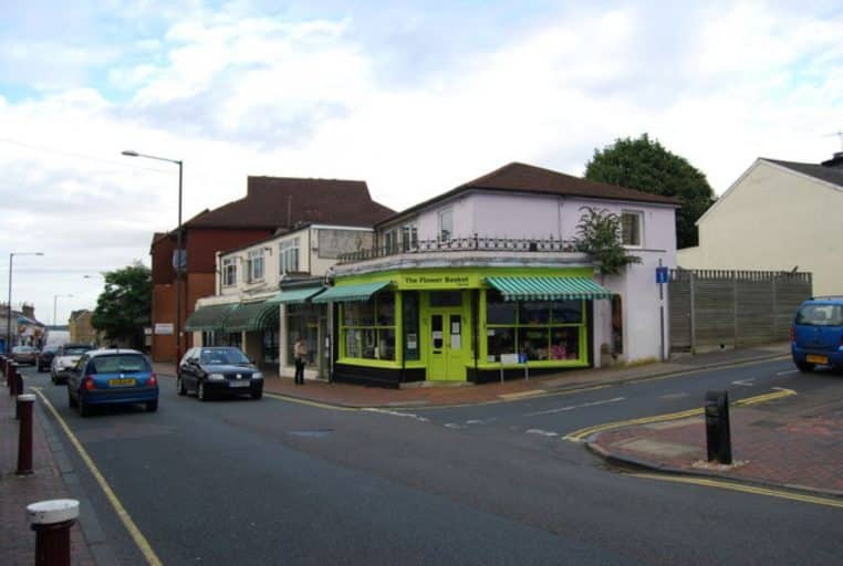 Coin de rue avec boutique de fleurs, devanture garnie et circulation piétonne, large angle horizontal pour une vue d’ensemble.